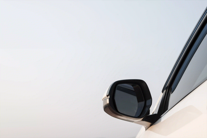 Close-up of a modern car side mirror on a white vehicle, emphasizing sleek automotive design and enhanced visibility features.