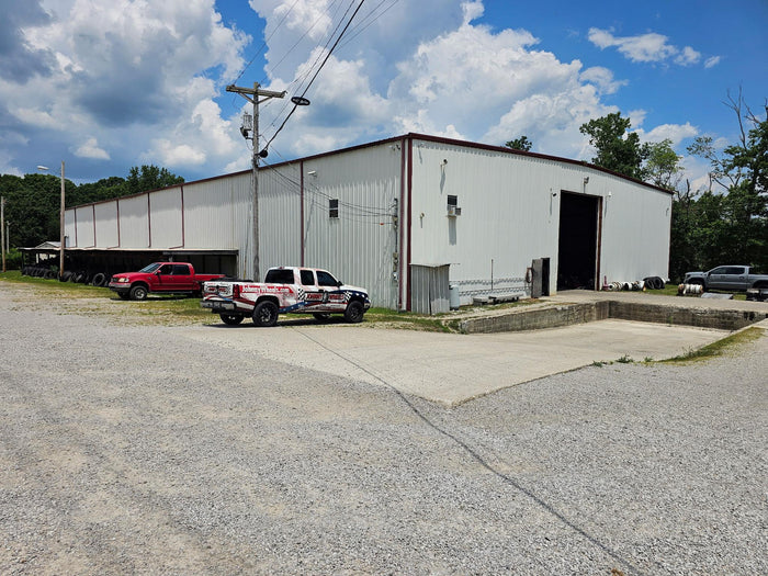 Johnny Wheels Tire Discounters Commercial building with open garage door, gravel lot, parked trucks, and tire inventory outside.