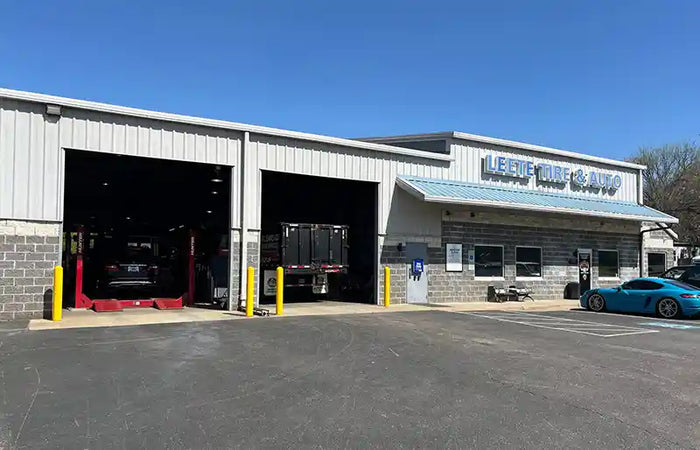 Leete Tire Discounters Commercial service center with open garage bays, vehicle lifts, and parked cars in front of the building.