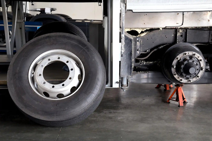 Commercial truck tire removed for repair, with wheel assembly on jack stands in service bay, highlighting tire maintenance and replacement.