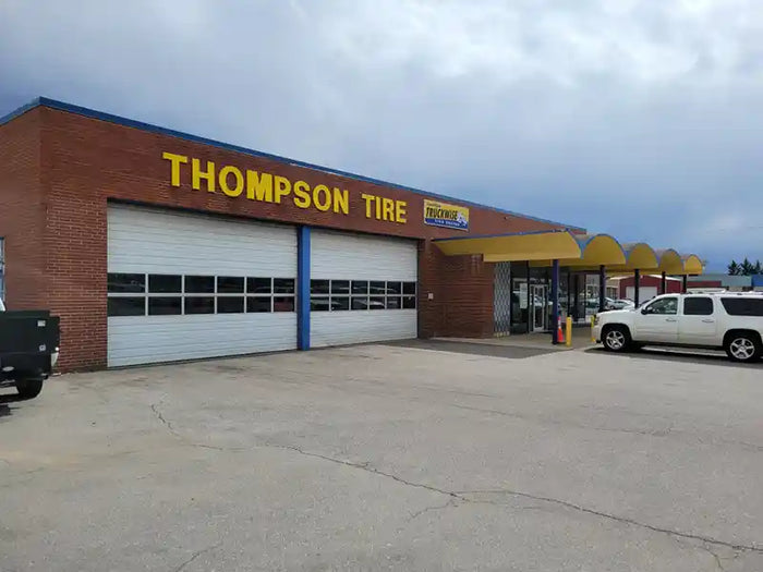 Thompson Tire Discounters Commercial building with brick exterior, yellow awning, and dual garage doors in front of a cloudy sky.