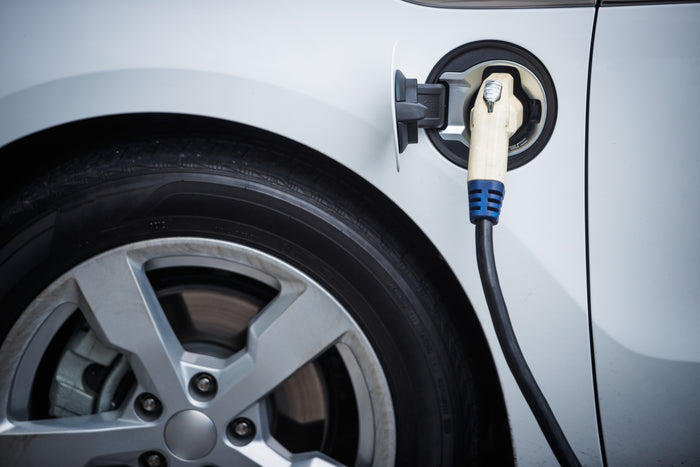 Close-up of electric vehicle plugged into a charging station, showing rear wheel and charge port on a white EV.