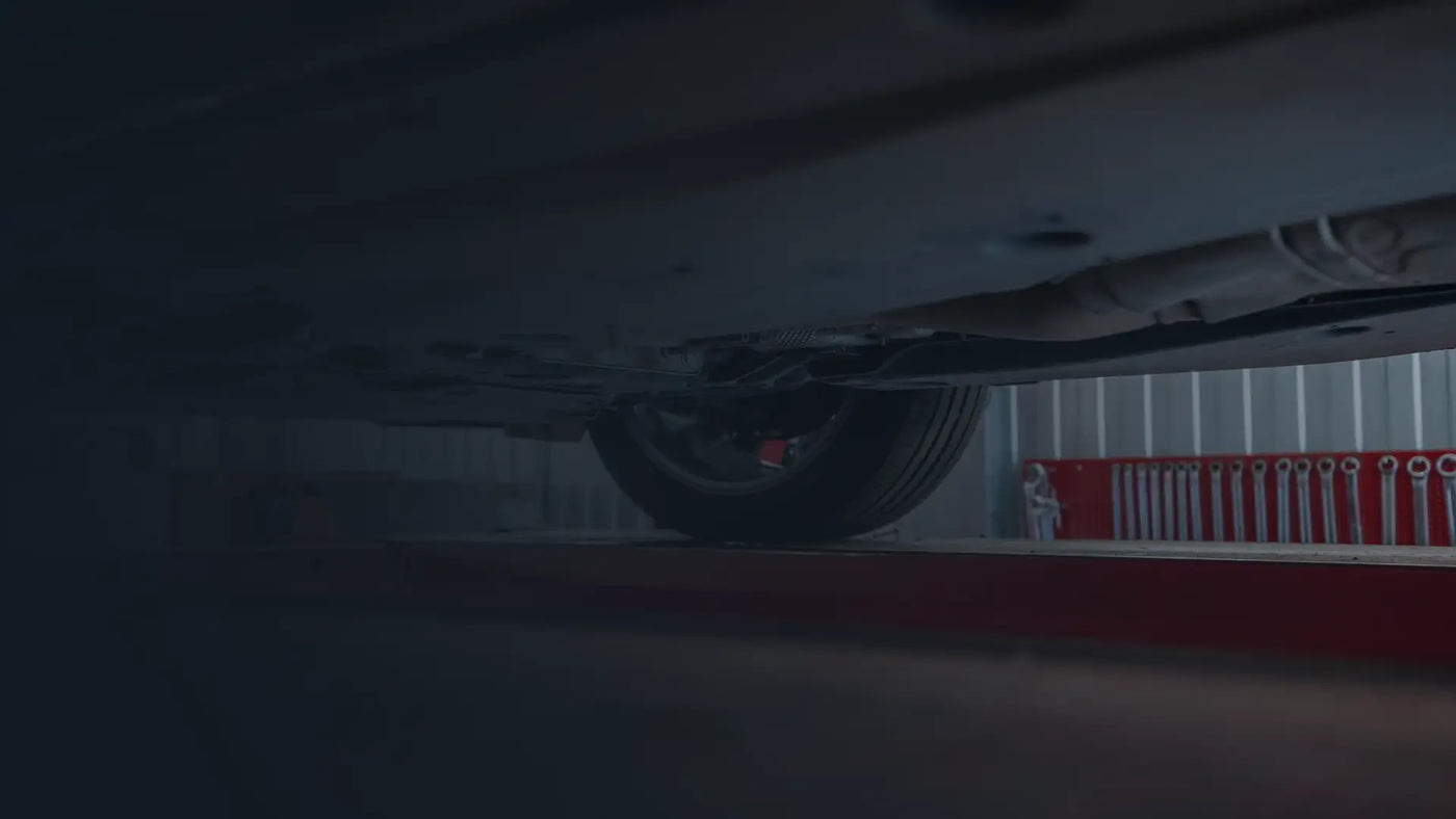 Underside of a vehicle on a red 4-post lift in a Tire Discounters shop