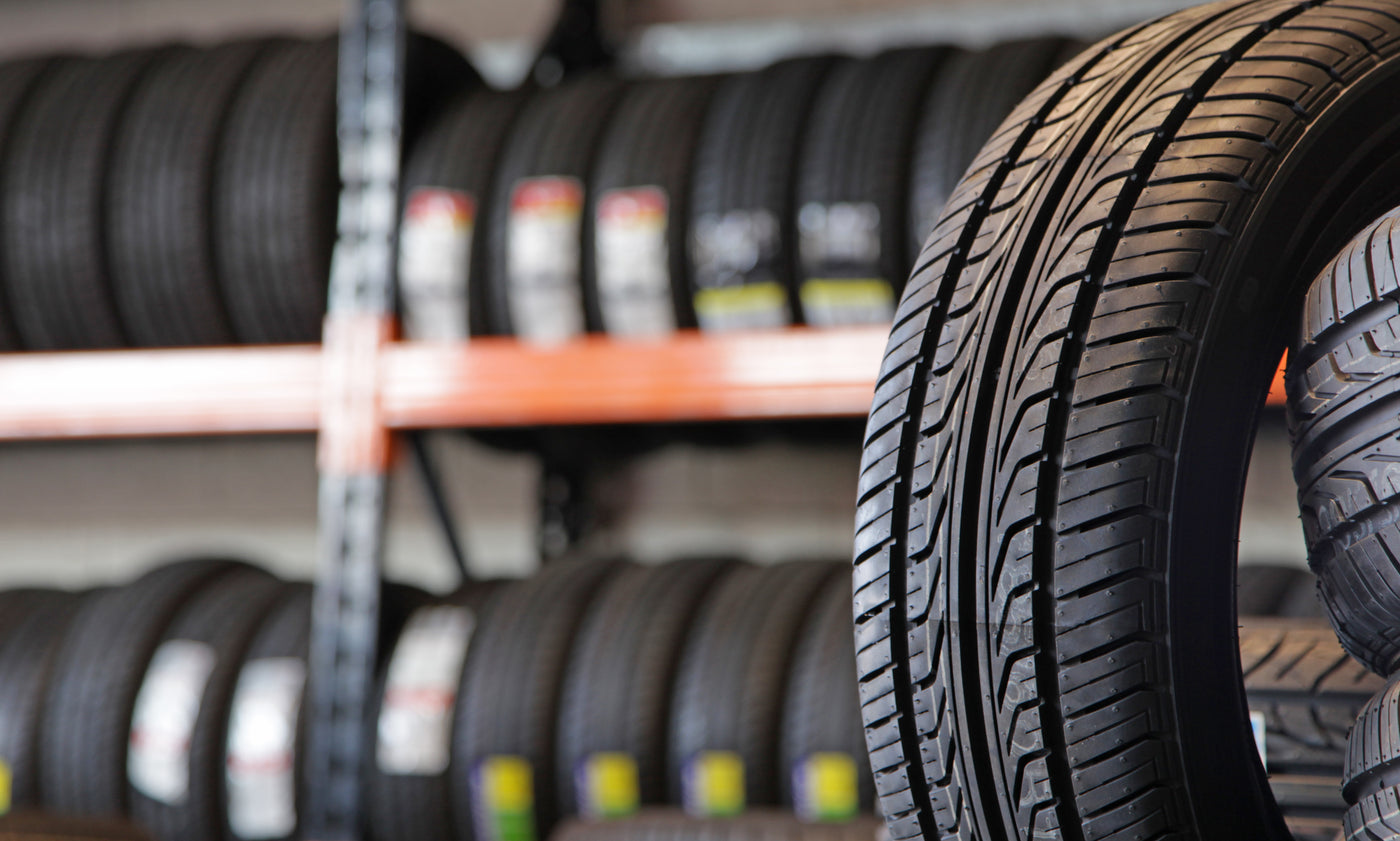 Close-up of new all-season tire tread with shelves of premium tires in background at a Tire Discounters store.