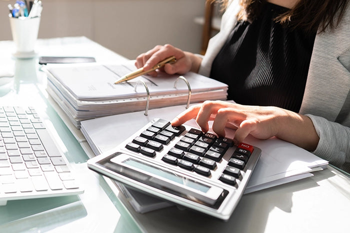 Close-up of businesswoman using calculator and reviewing financial documents for accounting, budgeting, or tax preparation tasks.
