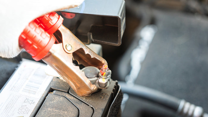 Close-up of jumper cable clamp connected to a car battery terminal during vehicle battery service or jump-start.