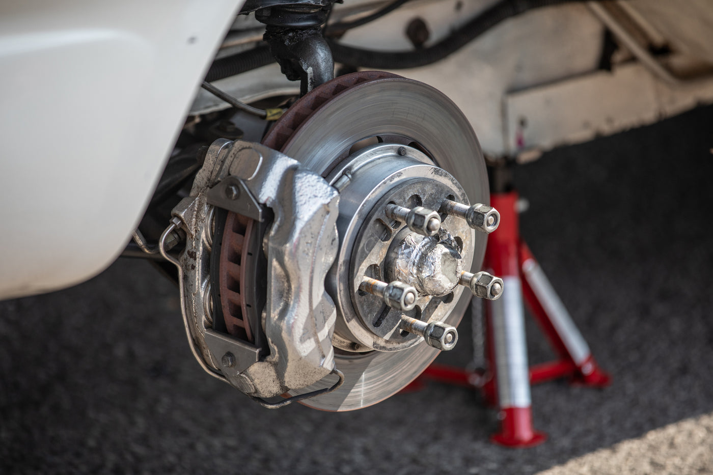 Exposed front disc brake and caliper assembly on a car lifted with a red jack stand.