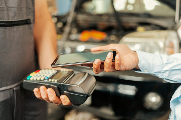 Customer making contactless payment with smartphone at auto repair shop checkout terminal.
