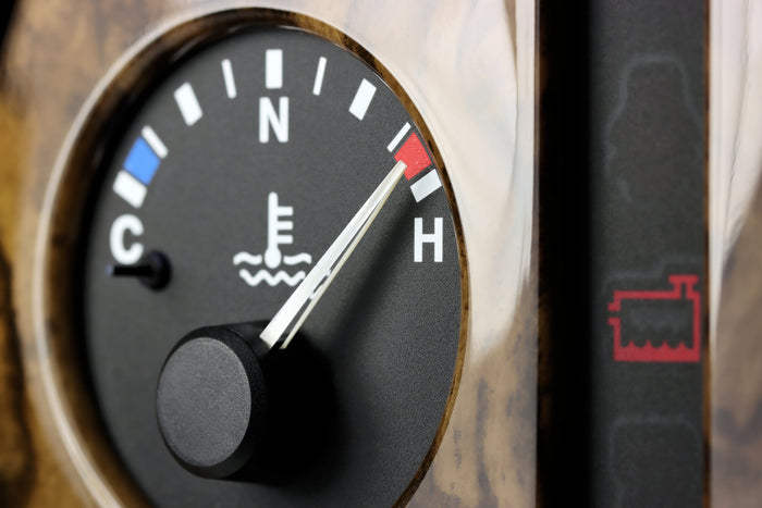 Close-up of a car's engine temperature gauge showing overheating with the needle pointing to the red "H" zone.
