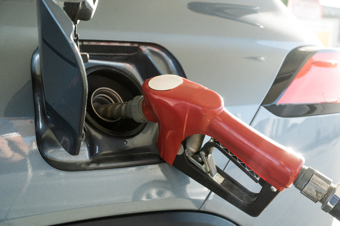 Close-up of a red gas pump nozzle inserted into a vehicle's fuel tank during refueling.