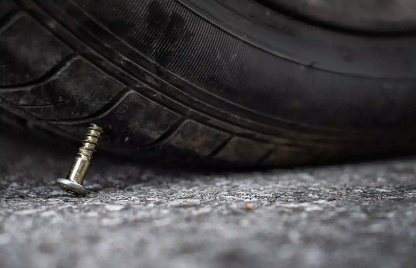 Close-up of a flat tire punctured by a screw, showing damage to the tread on a paved road.