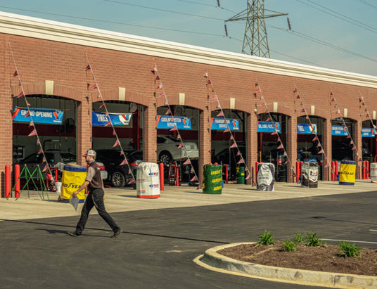 Tire Discounters service center with multiple open bays, technician walking, and grand opening banners; full-service tire and auto repair shop.