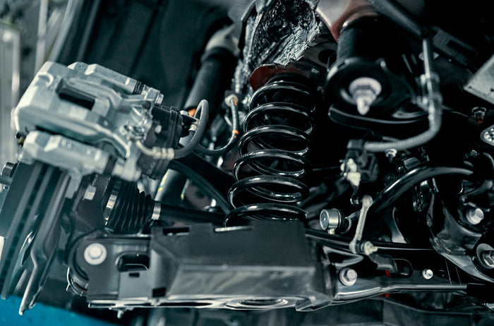 Close-up of vehicle suspension system with visible coil spring, control arm, and brake components in a service bay.