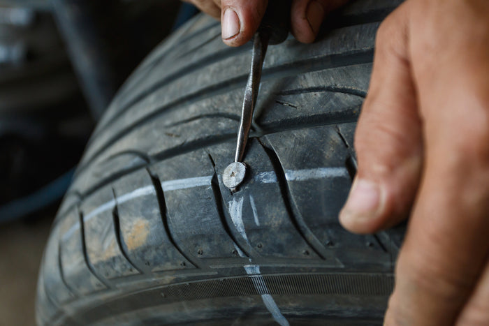 Close-up of a nail embedded in a car tire tread, being removed with a tool during flat tire repair service.