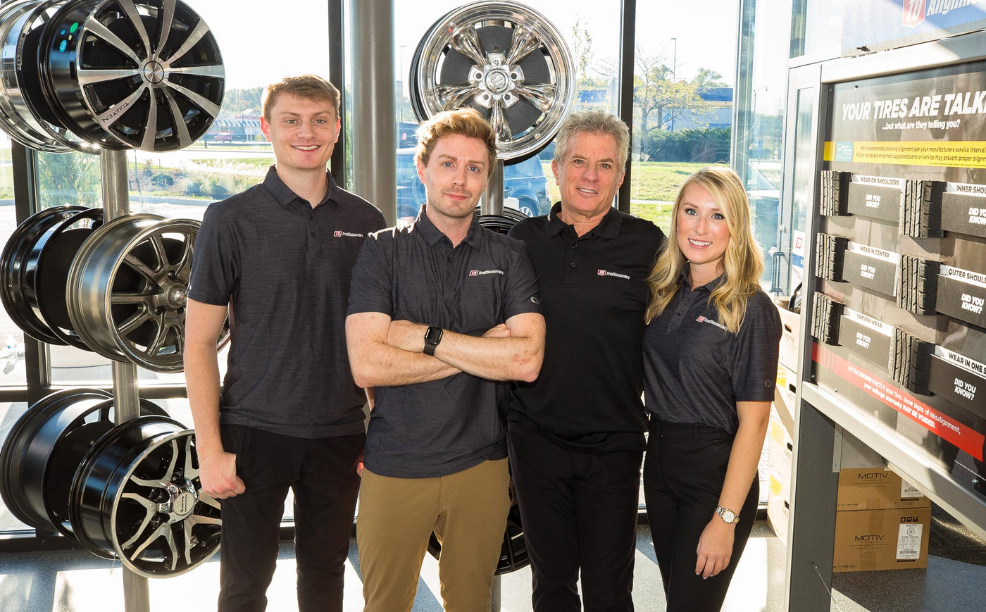 Four people standing in a tire store with tire displays in the background