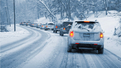 Snow-covered cars lined up on an icy road during a winter storm, promoting Tire Discounters free winter safety check.
