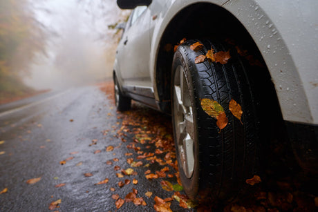 Car tire on wet autumn road with fallen leaves, symbolizing seasonal driving safety and traction in fall weather