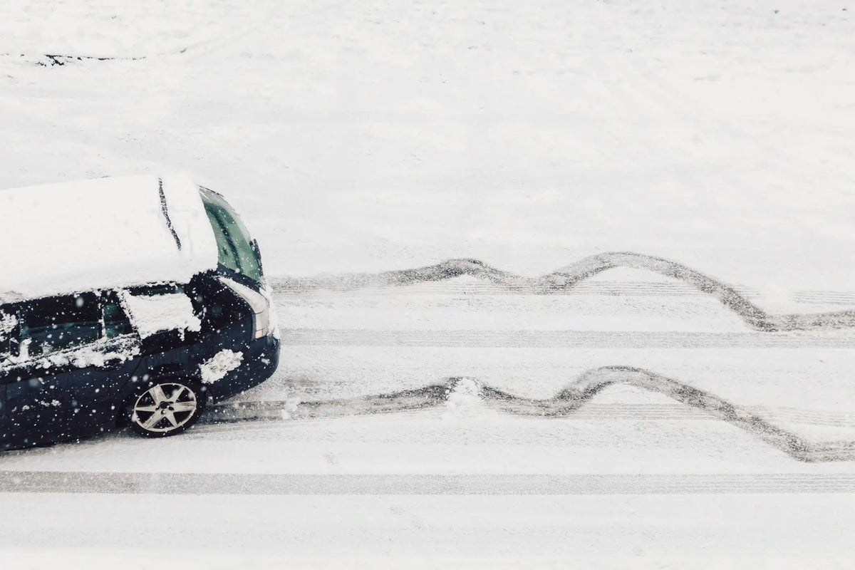 Car driving on a snow-covered road with tire tracks, illustrating winter driving conditions and the importance of proper tire traction