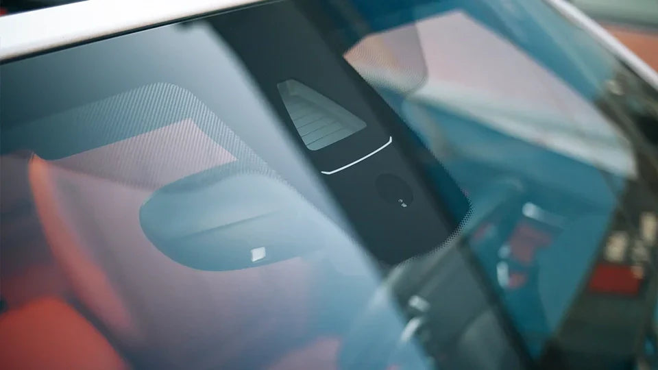 Close-up view through a car windshield showing advanced driver assistance system sensors near the rearview mirror