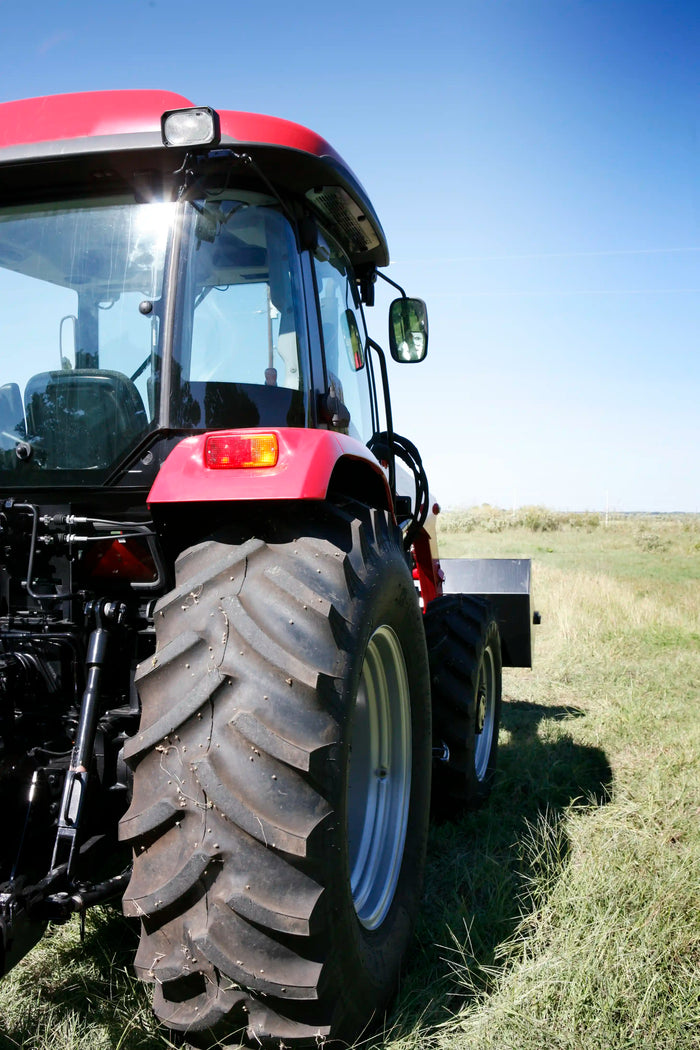 Close-up of rear tractor tire on grassy field under blue sky, showcasing durable agricultural tire tread for farming and heavy-duty use.
