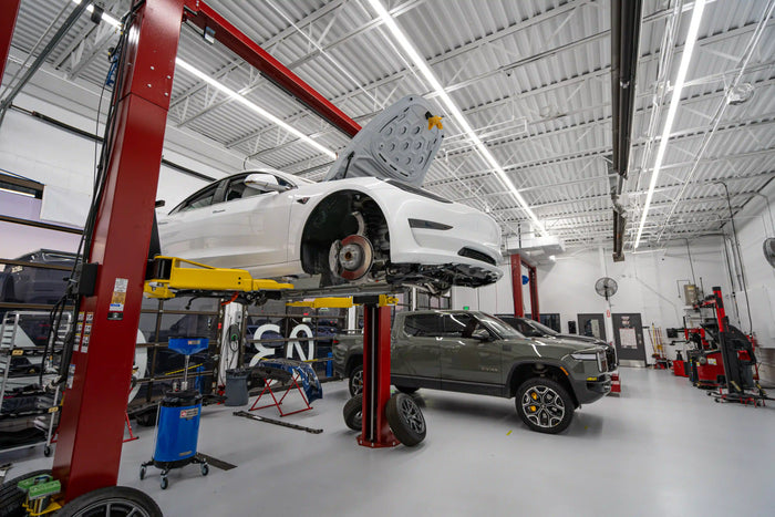 White Tesla on lift for brake or tire service in a clean auto repair shop with technician tools – Tire Discounters Electric Vehicle service center.