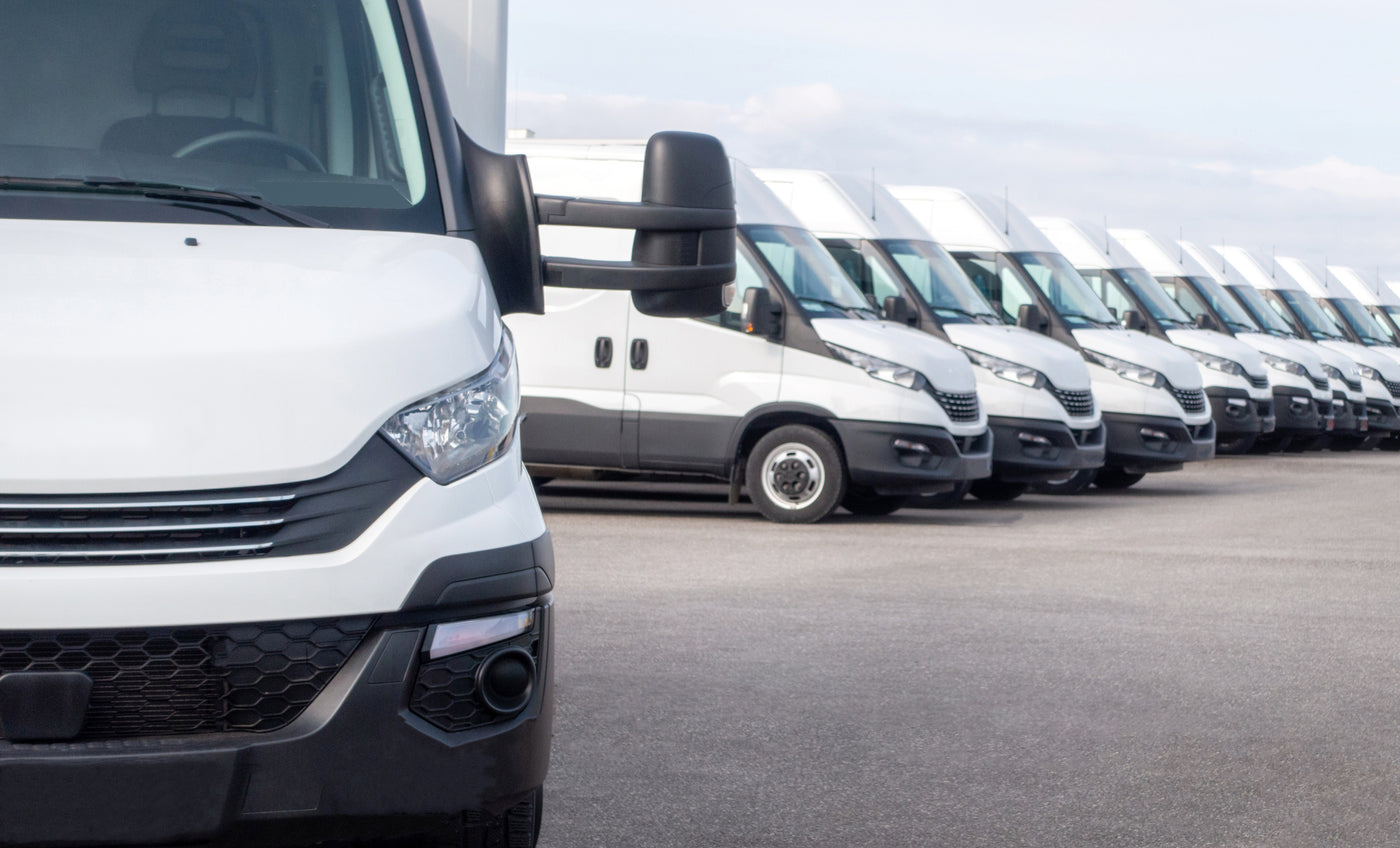 Row of white commercial cargo vans parked on a lot, ready for fleet service or delivery operations.