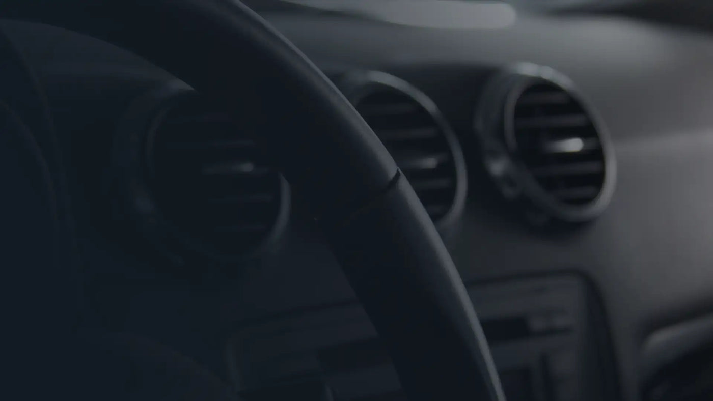 Car interior with steering wheel and dashboard with climate control vents in the background.