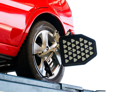 Wheel alignment in progress on a red car, showing sensor target mounted to rim on a vehicle lift.