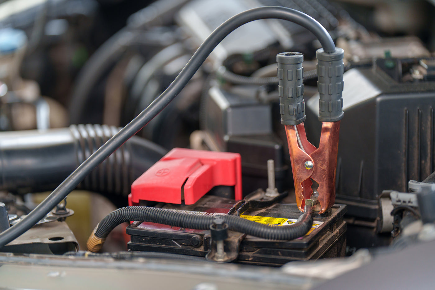 Close-up of a car battery with jumper cables attached, showing a vehicle jump-start procedure in progress.