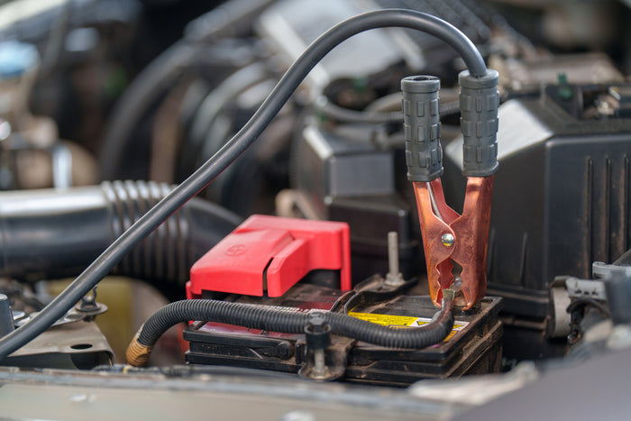 Close-up of a car battery with jumper cables attached, showing a vehicle jump-start procedure in progress.