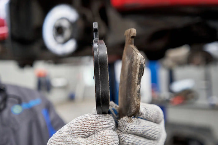 Technician comparing new vs worn brake pads to show brake wear and the need for timely brake replacement.