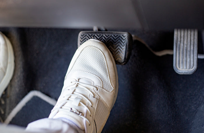 Driver's foot pressing the brake pedal inside a car, next to the gas pedal.