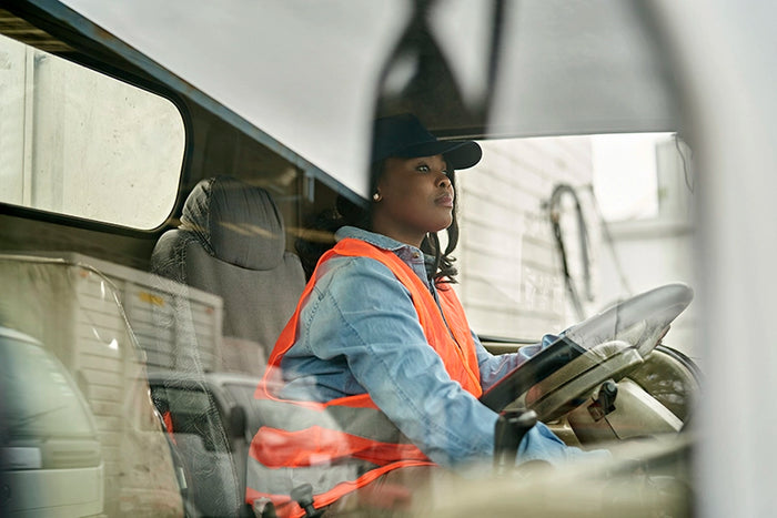 Female delivery truck driver in safety vest focused on the road while operating a commercial vehicle for logistics and shipping.