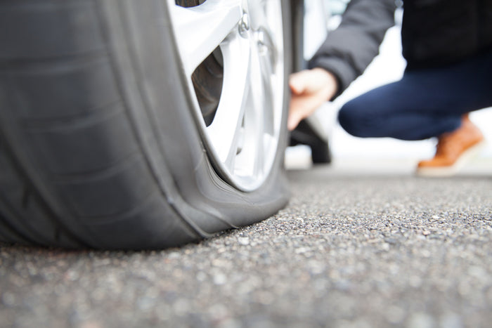 Close-up of flat car tire on roadside with person inspecting; Tire Discounters mobile tire repair and flat tire assistance service.
