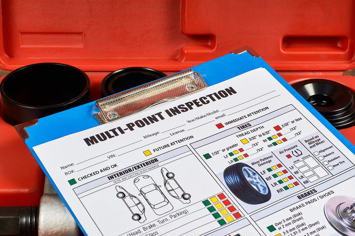 Vehicle multi-point inspection checklist on clipboard showing tire tread depth, brake pad condition, and service indicators.