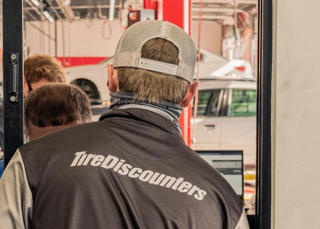 Tire Discounters technician in uniform inside auto repair shop, assisting with vehicle maintenance and customer service.