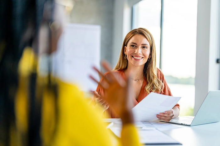 Smiling woman in professional setting holding documents during a business meeting or job interview in a bright office.
