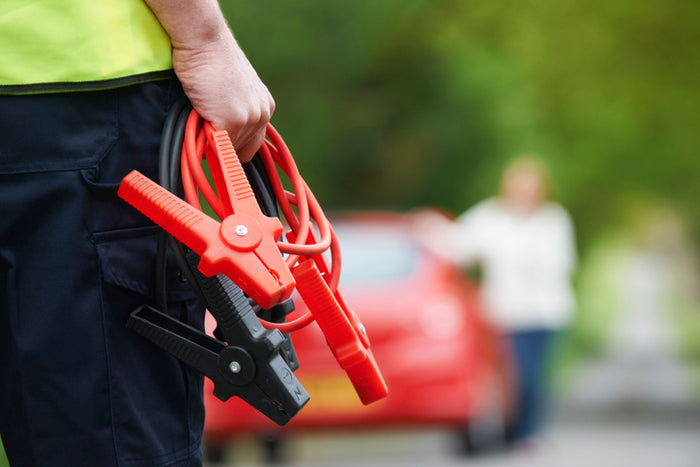 Technician holding jumper cables for roadside assistance; emergency car battery jump-start service with Tire Discounters.
