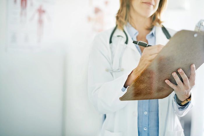 Female doctor in white coat writing on clipboard, representing expert medical care, patient health evaluations, and clinical services.