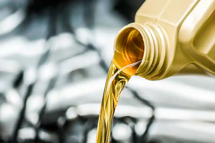 Close-up of golden motor oil being poured from a plastic container during an oil change.