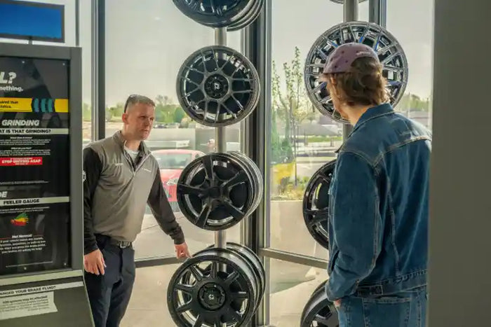 Tire Discounters team member helping customer choose custom wheels inside showroom with alloy rims on display.