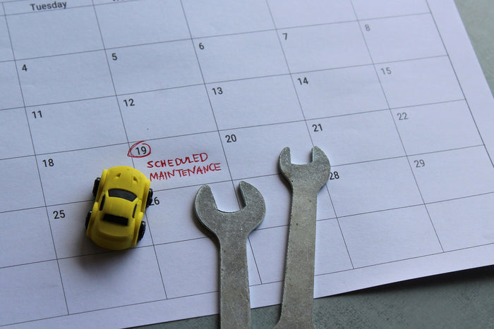 Small yellow toy car, wrenches, and a calendar with 'Scheduled Maintenance' written on it.