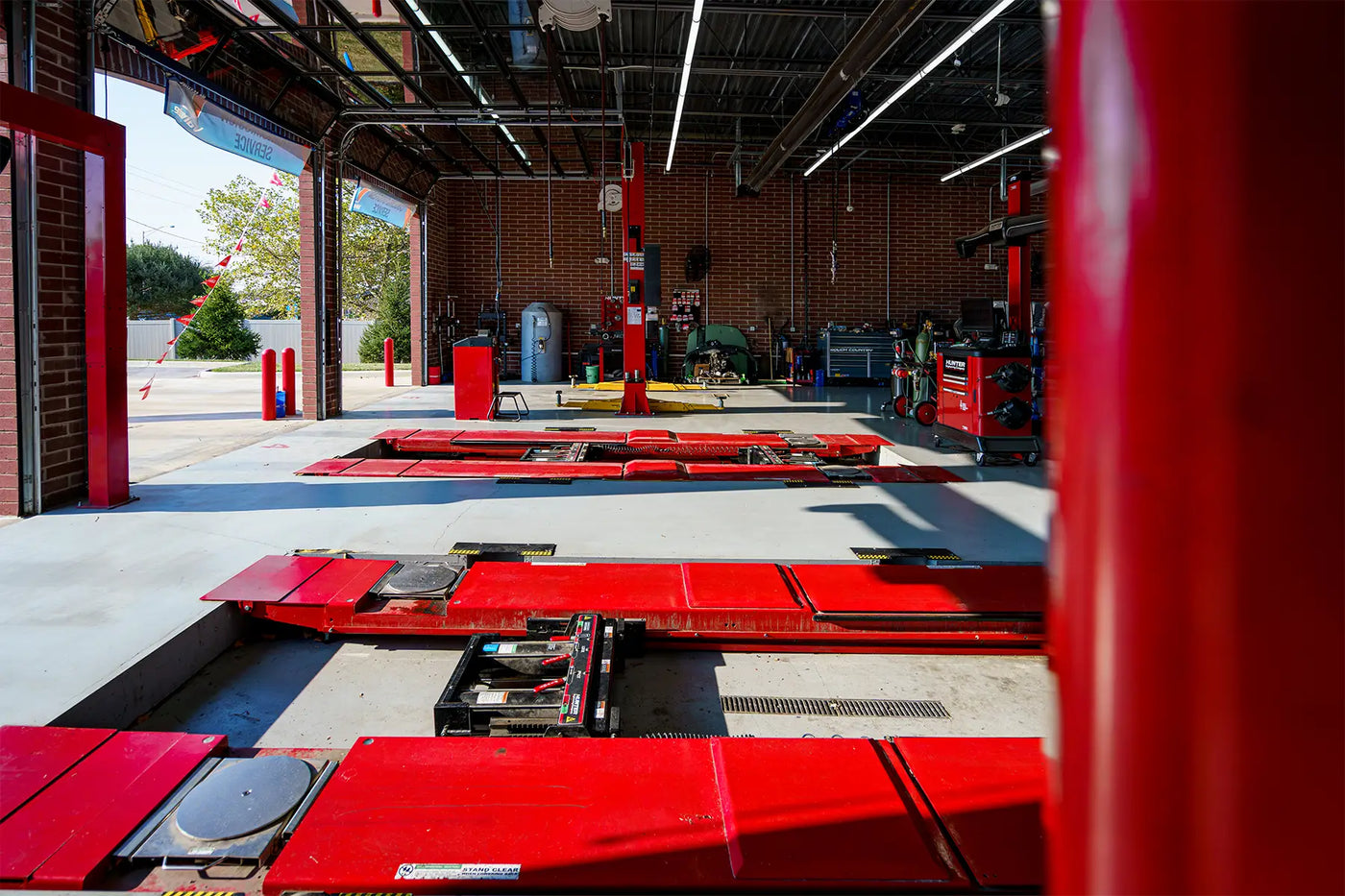 Modern auto repair shop with red alignment racks, open service bays, and diagnostic equipment at a tire and automotive service center.
