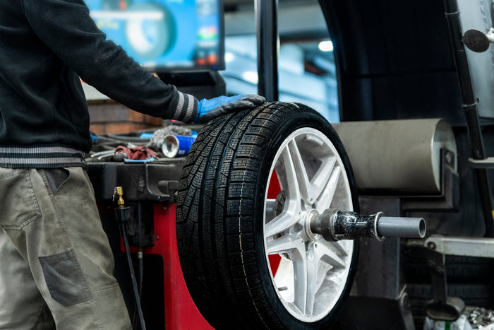 Technician using a tire balancing machine to ensure proper weight distribution on a mounted wheel and tire assembly.