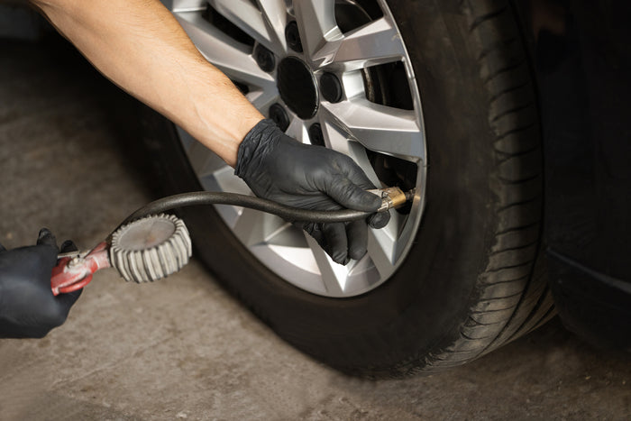 Technician inflating car tire with air hose and gauge to ensure proper tire pressure and safe driving conditions.