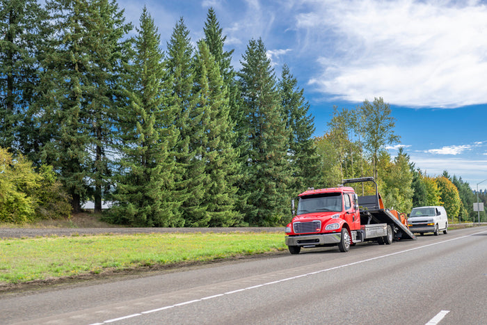 Tow truck assisting a stranded vehicle on a forest-lined highway – Tire Discounters roadside towing and emergency vehicle recovery service.