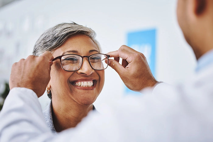 Woman smiling as she tries on new eyeglasses during vision care appointment, showcasing quality customer service and eyewear fitting.