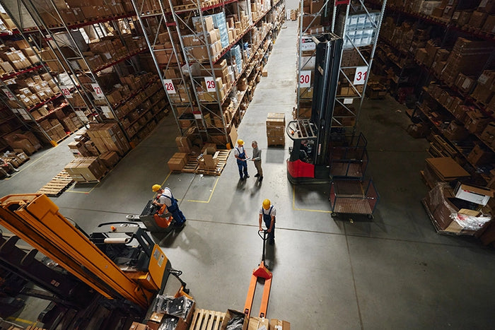 Warehouse workers with pallet jacks and forklifts managing inventory, showcasing logistics, fulfillment, and supply chain operations.