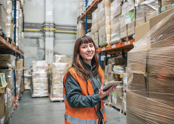 Warehouse employee with tablet smiling while managing inventory and logistics in a high-volume distribution center.