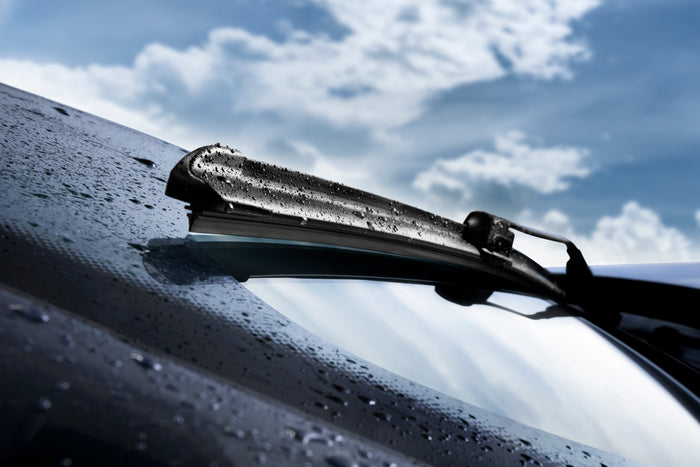 Car windshield wiper on a wet car window with a blue sky background
